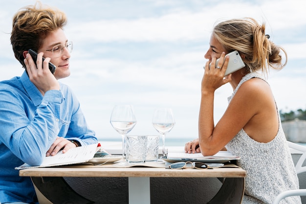 Jovem casal falando ao telefone, sentado em uma mesa de restaurante