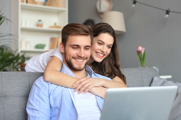 Jovem casal fazendo compras online em casa, usando um laptop no sofá.