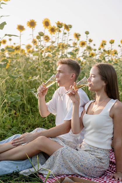 Jovem casal fazendo piquenique no campo de girassol ao pôr do sol