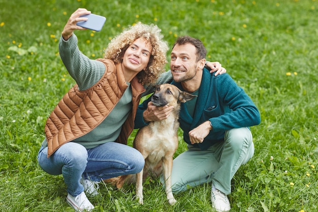 Jovem casal fazendo selfie no celular com seu animal de estimação ao ar livre