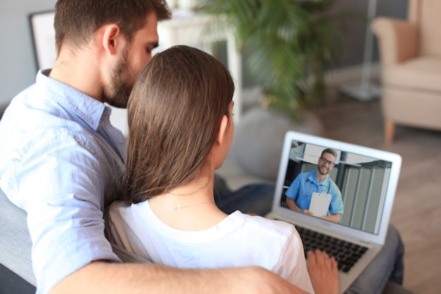 Jovem casal fazendo videoconferência com médicos no laptop. Coronavírus.