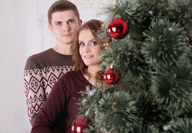 Jovem casal feliz abraçando perto da árvore de Natal comemorando o ano novo juntos sorrindo