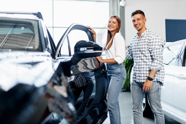 Jovem casal feliz acaba de comprar um carro novo em uma concessionária