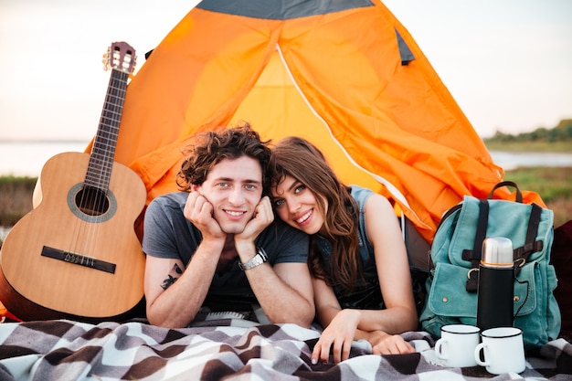 Jovem casal feliz acampando na praia, deitado na barraca