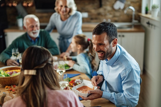 Foto jovem casal feliz almoçando em família na sala de jantar. o foco está no homem passando comida para sua esposa.