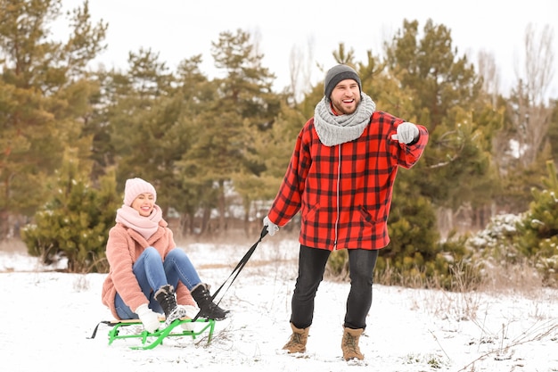Jovem casal feliz andando de trenó no parque no dia de inverno