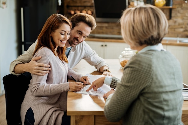 Jovem casal feliz assinando um contrato durante uma reunião com consultor financeiro em casa