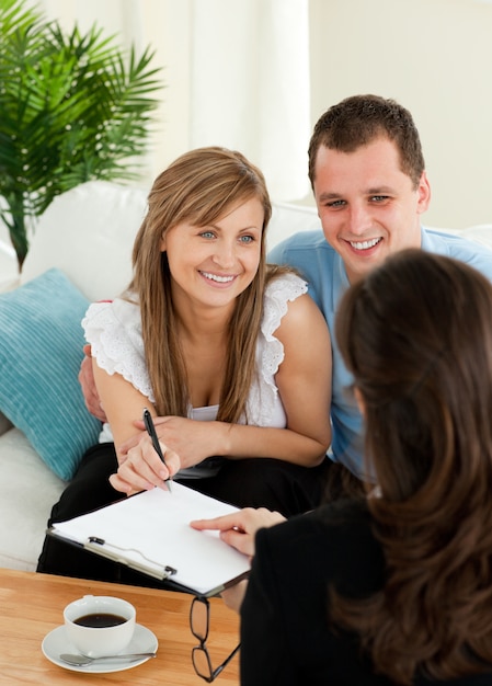 Foto jovem casal feliz assinando um contrato sentado na sala de estar