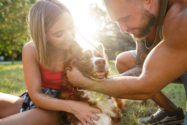 Foto jovem casal feliz brincando com seu cachorro sorrindo no parque