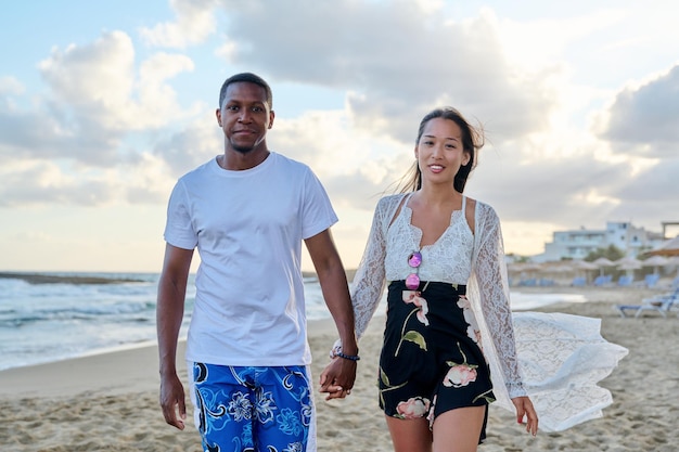 Jovem casal feliz caminhando na praia de mãos dadas