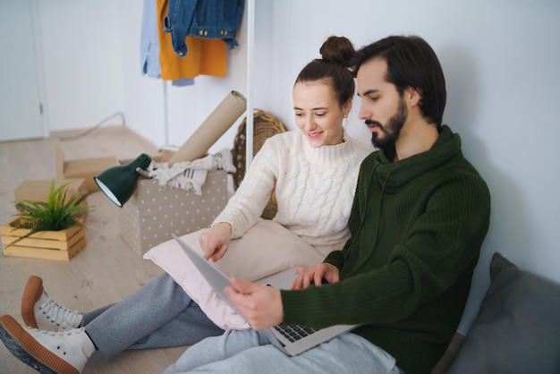 Jovem casal feliz com laptop e caixas, movendo-se em um novo conceito de apartamento, novo lar e realocação.