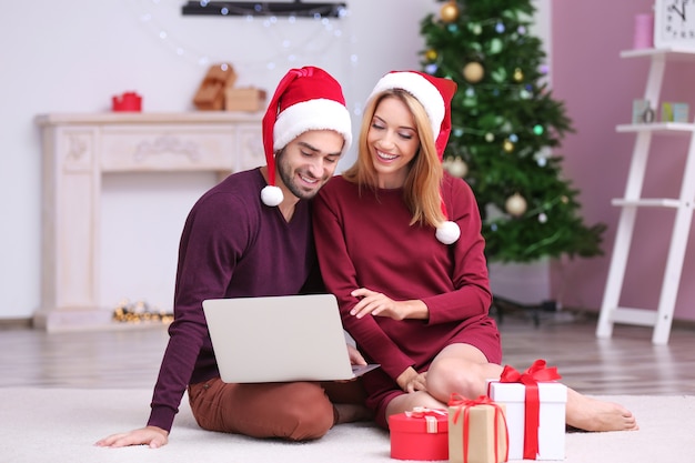 Jovem casal feliz com o laptop em casa. Conceito de natal