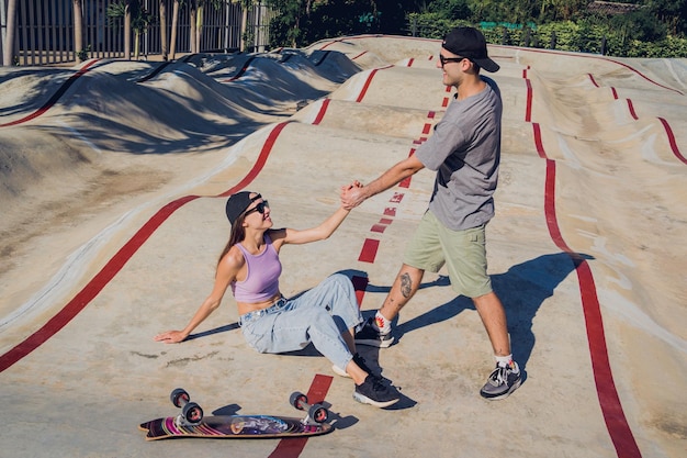 Jovem casal feliz com skates desfruta de longboard no skatepark