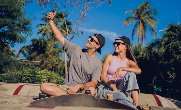 Jovem casal feliz com skates tirando selfie no skatepark