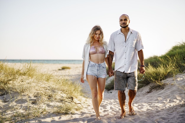 Jovem casal feliz de mãos dadas e caminhando juntos para a praia num dia de verão