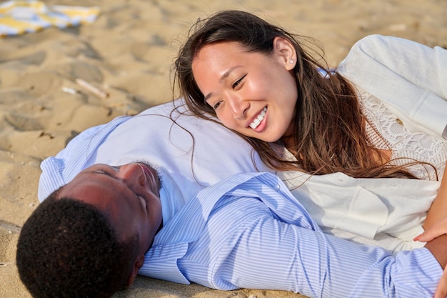 Jovem casal feliz deitado na areia conversando curtindo os sentidos juntos