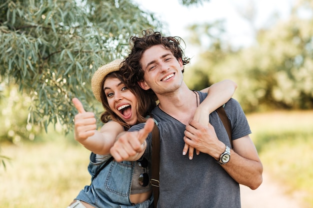 Foto jovem casal feliz e alegre mostrando os polegares e se abraçando sobre o fundo da floresta