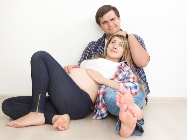 Jovem casal feliz esperando bebê posando no chão da sala de estar