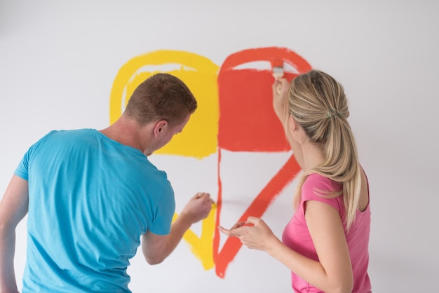 Jovem casal feliz está pintando um coração na parede enquanto faz reparos em casa.