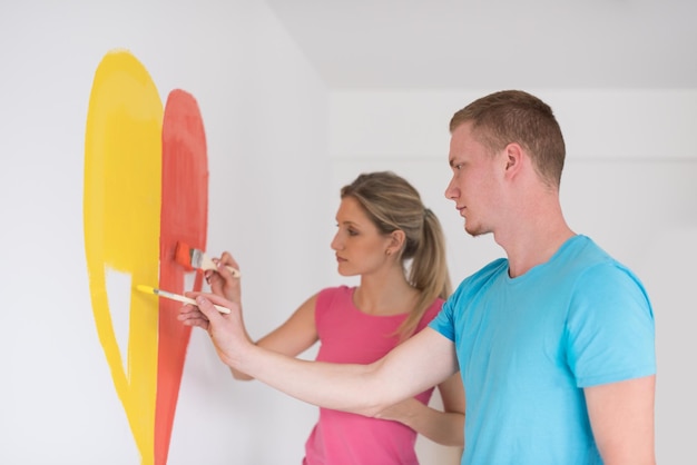 Jovem casal feliz está pintando um coração na parede enquanto faz reparos em casa.