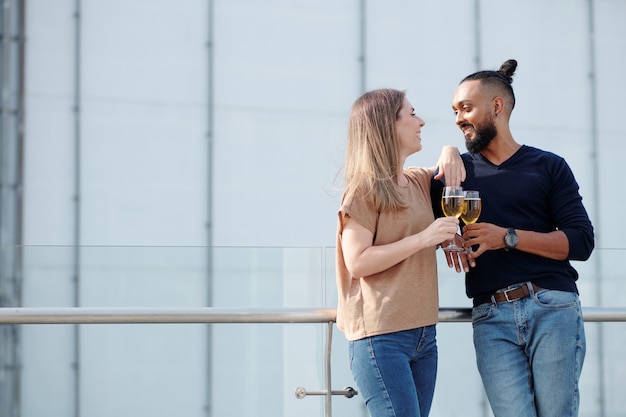 Foto jovem casal feliz flertando, conversando e brincando ao beber champanhe em uma festa no telhado
