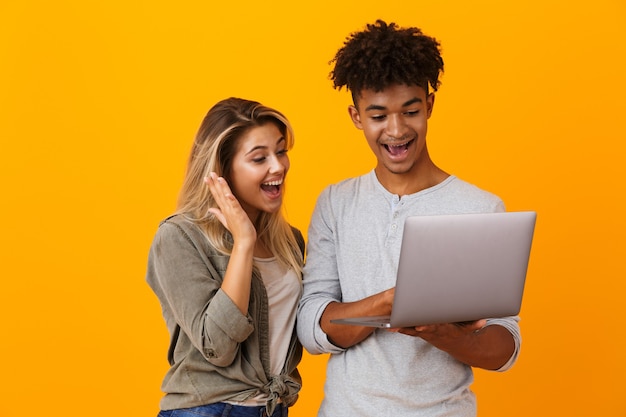 Jovem casal feliz, isolado na parede amarela, usando um computador laptop