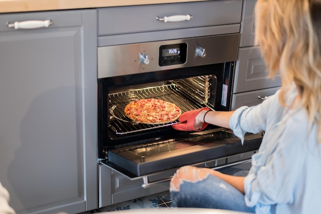 Jovem casal feliz jantando em casa e uma jovem loira linda tirando uma pizza do forno