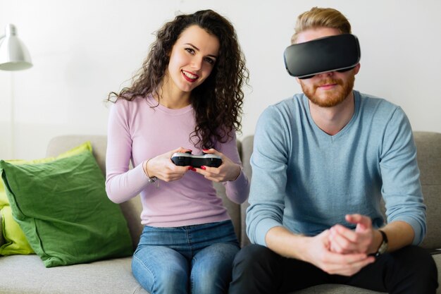Jovem casal feliz jogando videogame com fones de ouvido de realidade virtual em casa