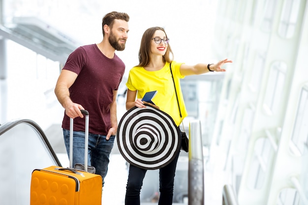 Jovem casal feliz levantando-se com a bagagem na escada rolante para a área de embarque do aeroporto durante as férias de verão