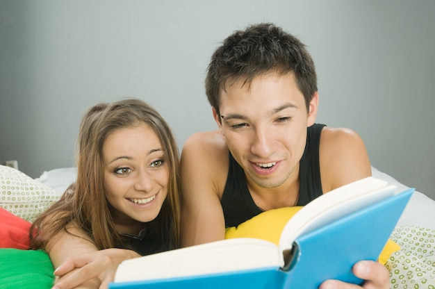 Jovem casal feliz na cama lendo um livro