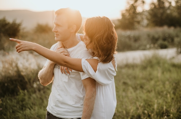 Jovem casal feliz no fundo da natureza. menina mostrando com a mão. conceito de amor