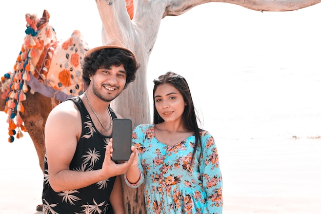 jovem casal feliz pose frontal segurando o celphone na praia modelo paquistanês indiano