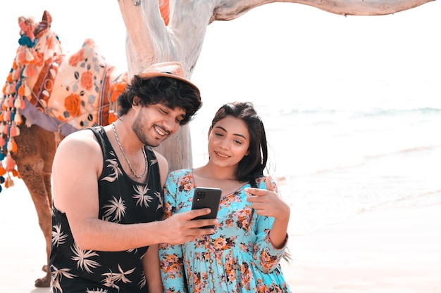 jovem casal feliz pose frontal usando celphone na praia modelo paquistanês indiano