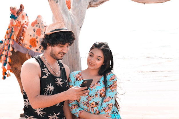 jovem casal feliz pose frontal usando celphone na praia modelo paquistanês indiano