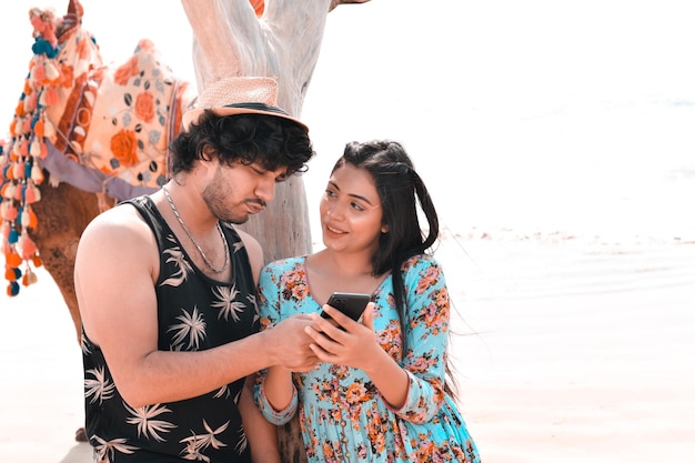 jovem casal feliz pose frontal usando celphone na praia modelo paquistanês indiano