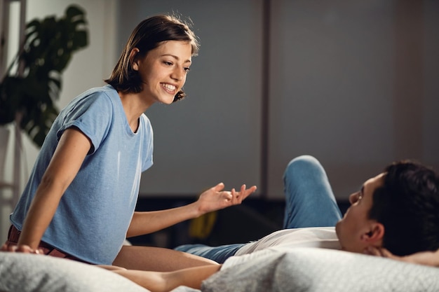 Jovem casal feliz relaxando na cama e conversando um com o outro O foco está na mulher