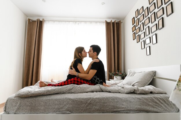 Jovem casal feliz se beijando na cama com roupas de pijama