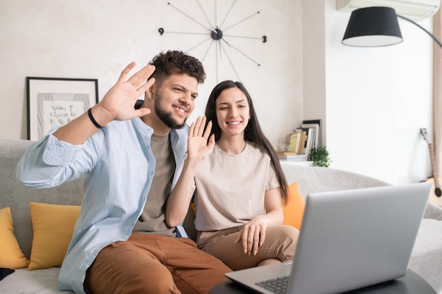 Jovem casal feliz se comunicando por vídeo chat em frente ao laptop