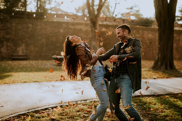 Jovem casal feliz se divertindo com folhas de outono no parque