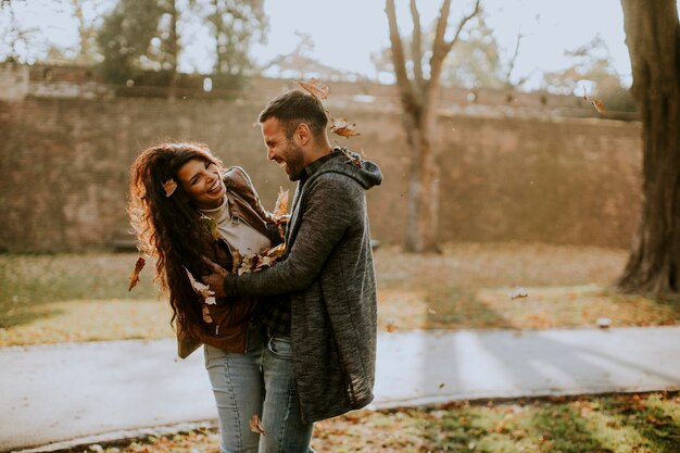 Jovem casal feliz se divertindo com folhas de outono no parque