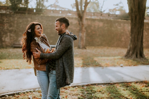 Jovem casal feliz se divertindo com folhas de outono no parque