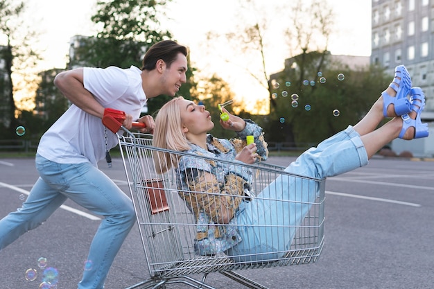 Foto jovem casal feliz se divertindo com um carrinho de compras no estacionamento de um supermercado