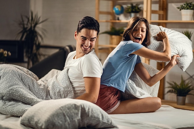 Jovem casal feliz se divertindo durante uma luta de travesseiros no quarto