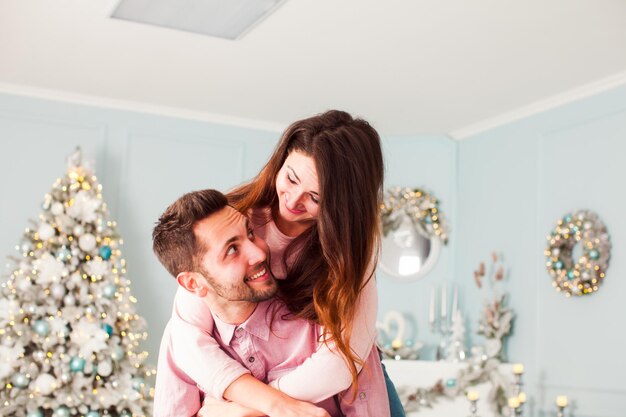 Jovem casal feliz se divertindo e abraçando perto da árvore de natal