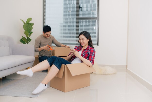 Jovem casal feliz se mudando para seu novo apartamento, se divertindo e andando em caixas de papelão na nova casa