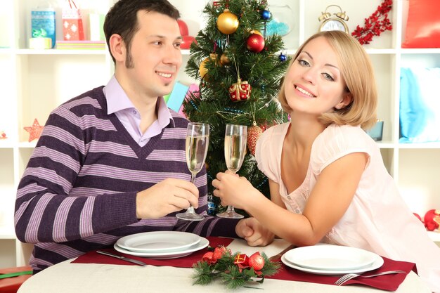 Jovem casal feliz segurando taças com champanhe na mesa perto da árvore de Natal