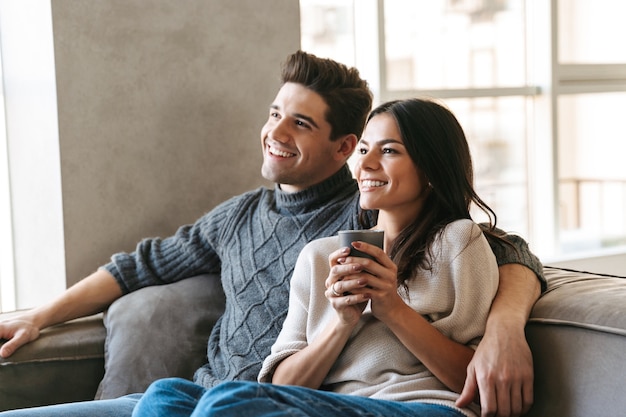 Jovem casal feliz sentado em um sofá em casa, assistindo TV