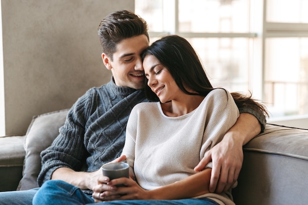 Jovem casal feliz sentado em um sofá em casa, assistindo tv