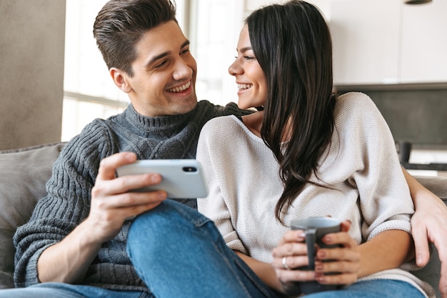 Jovem casal feliz sentado em um sofá em casa, bebendo chá