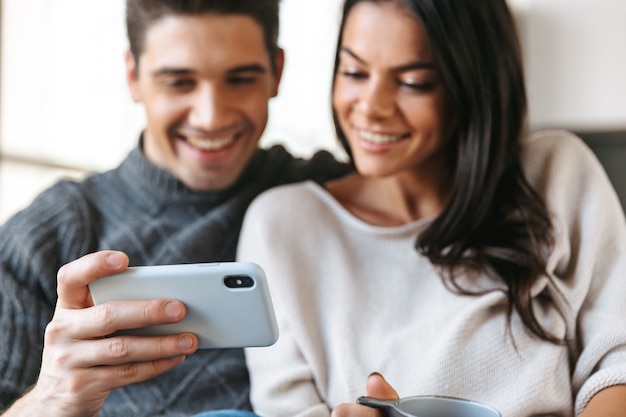 Jovem casal feliz sentado em um sofá em casa, bebendo chá